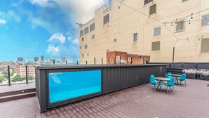 Eine Dachterrasse mit blauer Markise, Sitzgelegenheiten im Freien und Blick auf die Stadt.