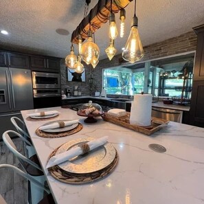 A modern kitchen with a marble countertop, stainless steel appliances, and a unique light fixture.
