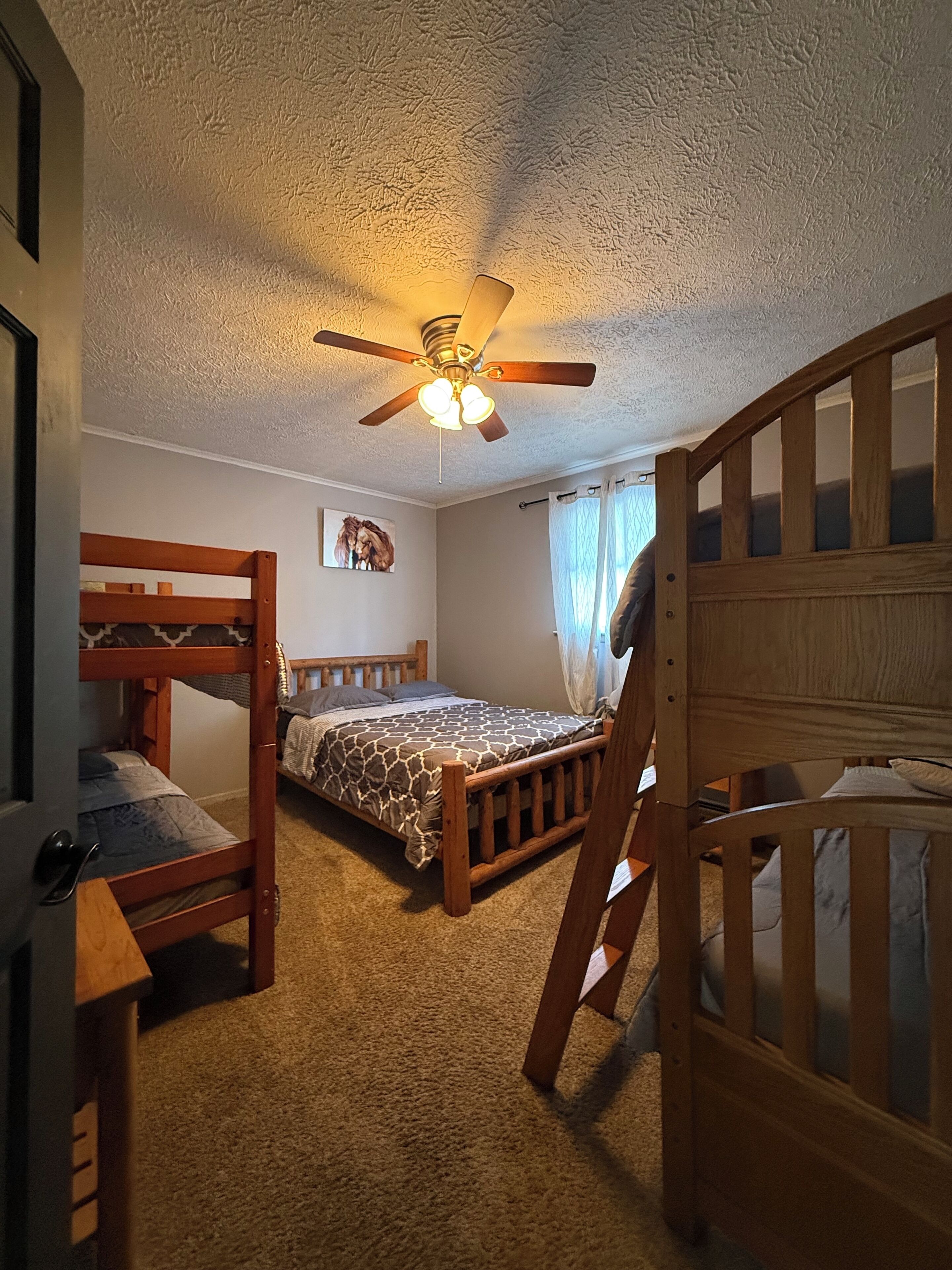 Une chambre avec des lits superposés, un ventilateur de plafond et un lit recouvert d’une couvre-lit à motifs.