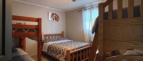 Une chambre avec des lits superposés, un ventilateur de plafond et un lit recouvert d’une couvre-lit à motifs.