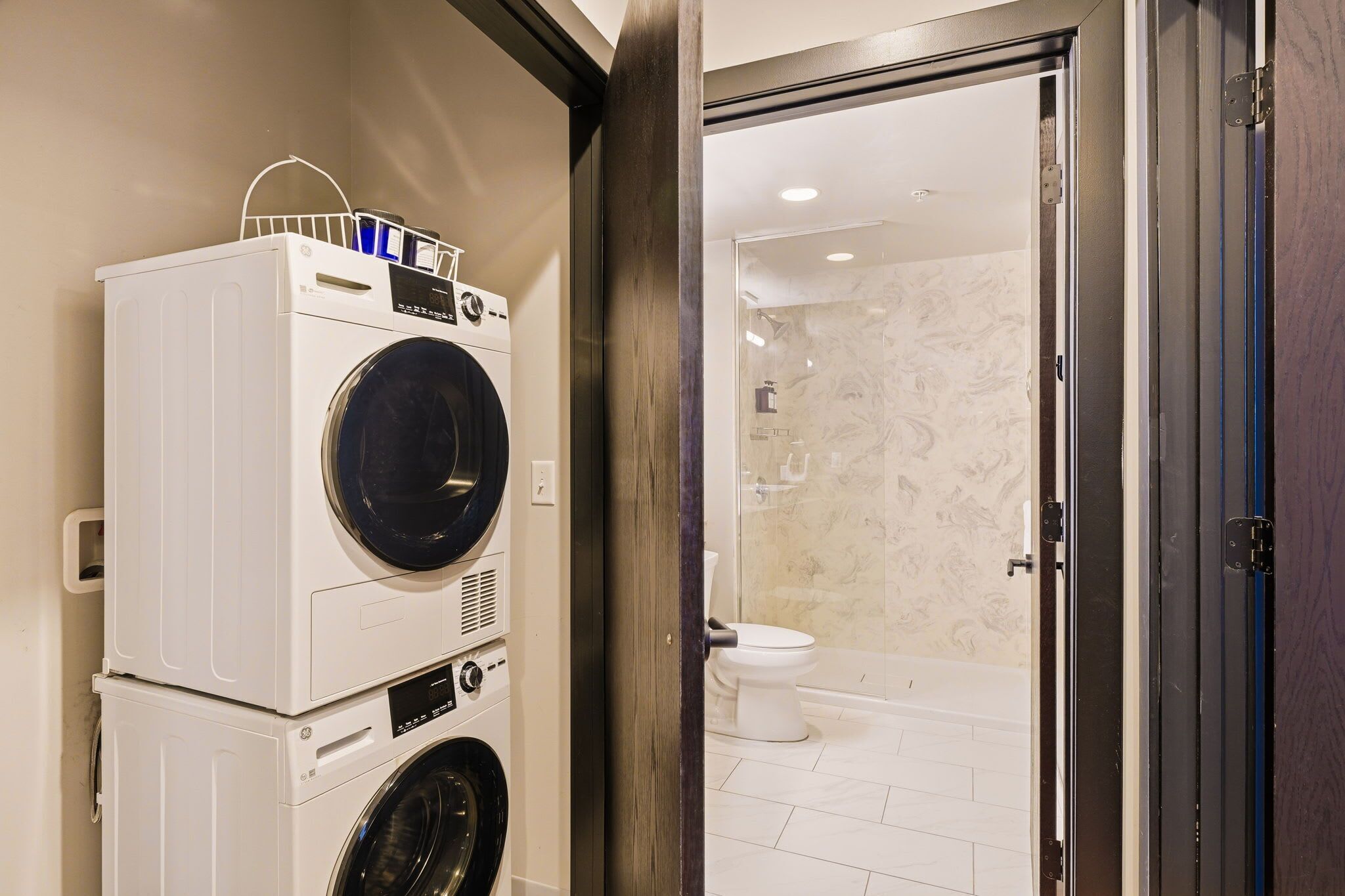 A laundry area with stacked washers and dryers, a bathroom with a toilet and shower, and a wooden door frame.