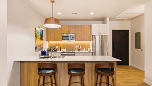 A modern kitchen with a large island, bar stools, a microwave, and a refrigerator.
