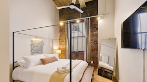 A modern bedroom with a four-poster bed, a bench, a large mirror, and a brick wall.