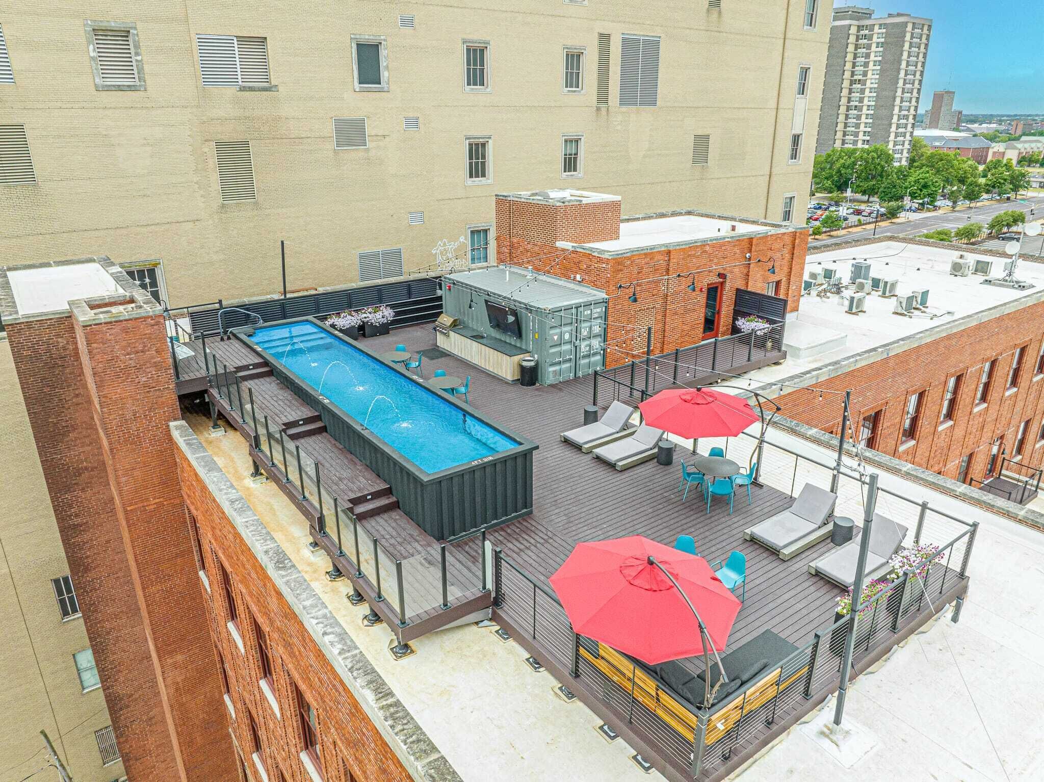 Un espace piscine aménagé sur le toit, avec une longue piscine rectangulaire, des chaises longues et des parasols.