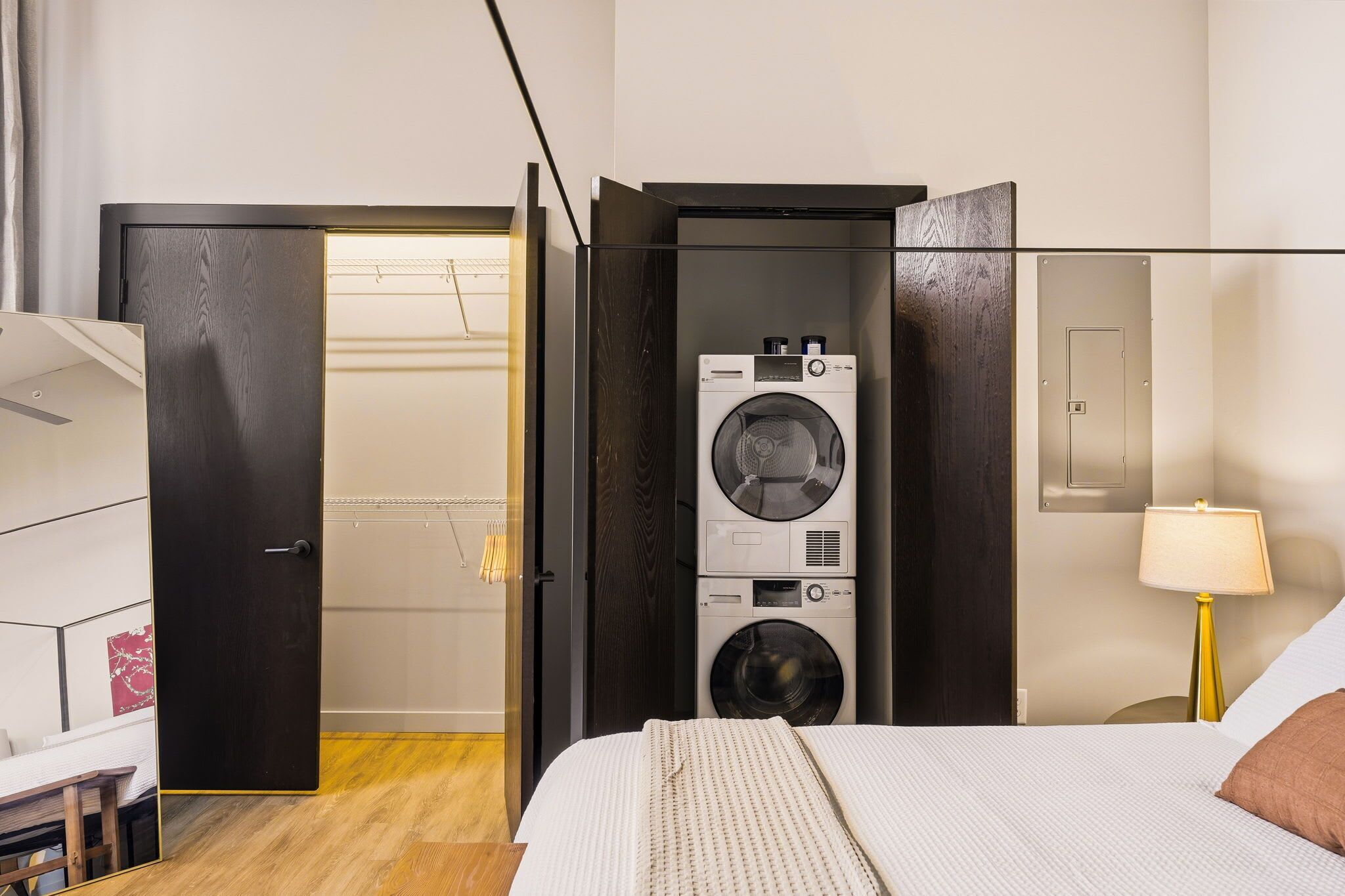 A hotel room with a bed, a washing machine, a desk, and a lamp.
