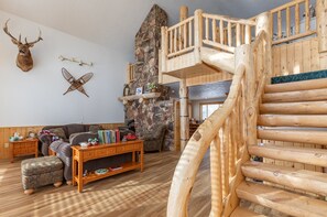 A rustic interior with a wooden staircase, a stone fireplace, and a deer head mounted on the wall. - Chester Currents (St. Anthony)