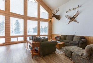 A log cabin interior with a large window, a mounted deer head, a decorative airplane, and a cozy seating area. - Chester Currents (St. Anthony)