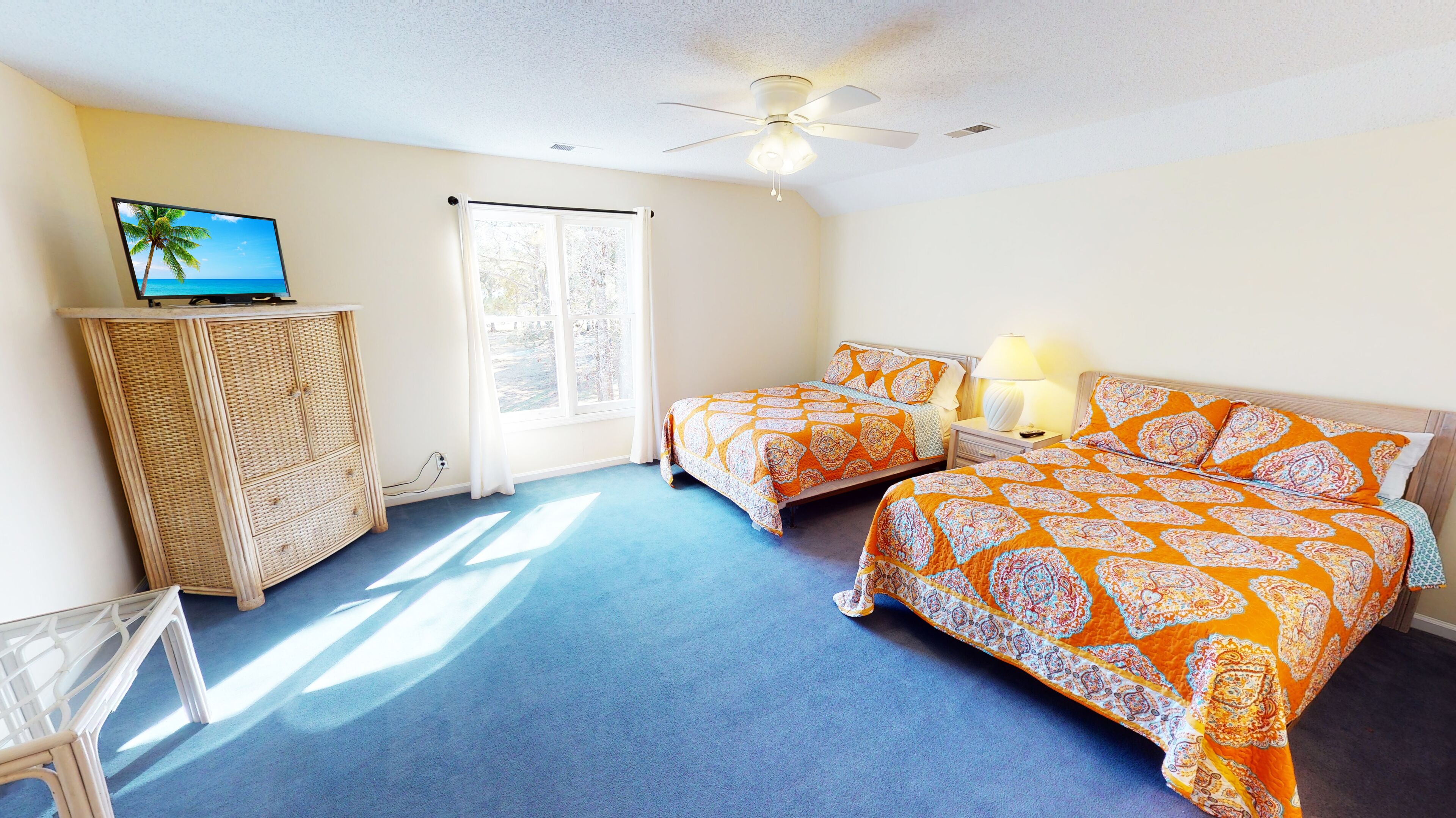 A bedroom with two beds, a ceiling fan, a TV on a cabinet, and a window with curtains.