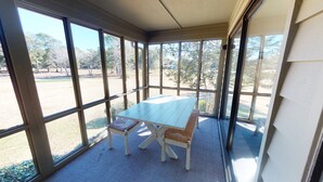 A covered patio with a table and chairs, large windows, and a view of the outdoors. - Club Villas Unit 4A (Sunset Beach)