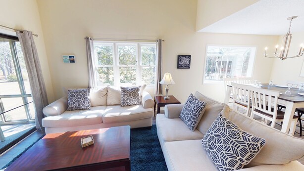A living room with a sofa set, a coffee table, a dining table with chairs, and a chandelier. - Club Villas Unit 4A (Sunset Beach)