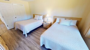 A hotel room with two single beds, a nightstand with a lamp, and a wooden floor. - Club Villas Unit 4A (Sunset Beach)