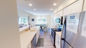 A modern kitchen with a dining area, large windows, and a view of the outdoors. - Club Villas Unit 4A (Sunset Beach)