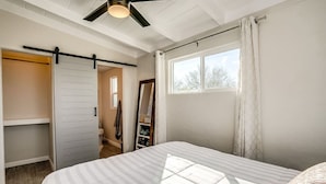 Un dormitorio con cama, armario corredero, ventana con cortinas y ventilador de techo.