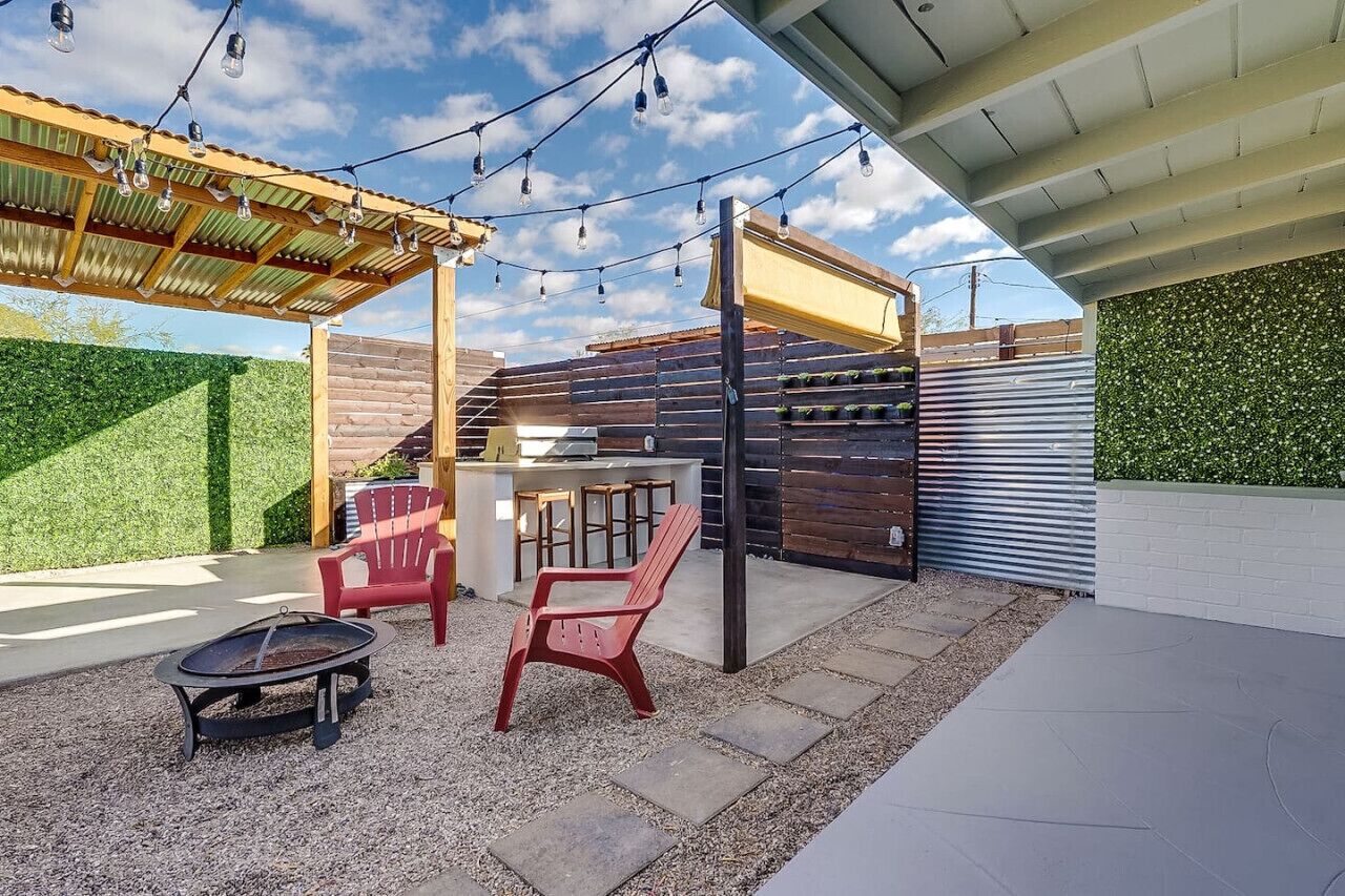 Een terras buiten met een pergola, lichtjes, een vuurkorf en rode stoelen.