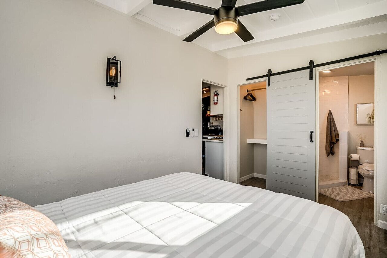A bedroom with a bed, a ceiling fan, a wardrobe, and a bathroom visible through an open door.