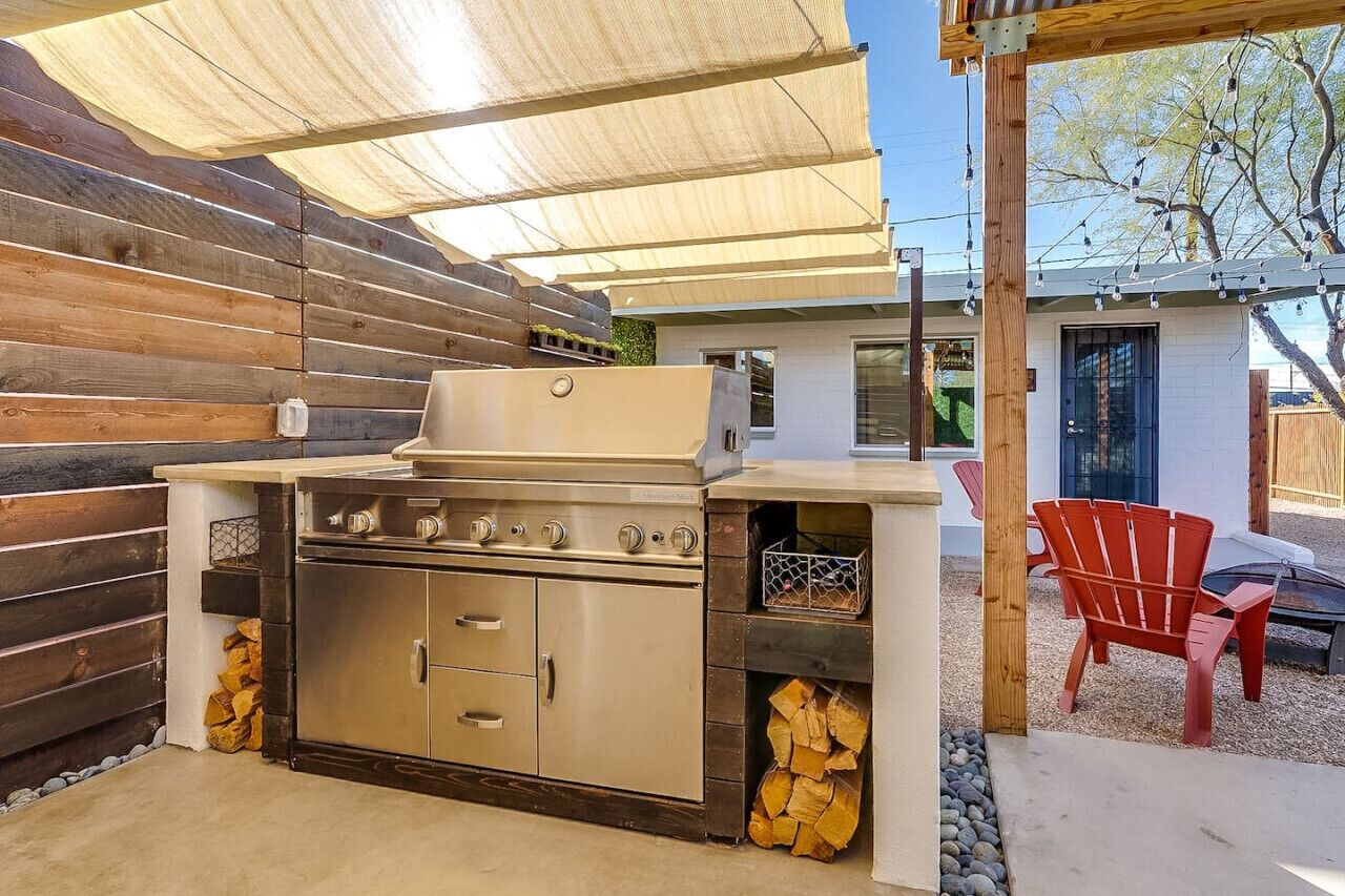 An outdoor kitchen with a grill, storage cabinets, and a covered seating area with chairs.