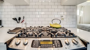 Una cocina moderna con estufa a gas, un reloj digital y una tetera sobre la encimera.