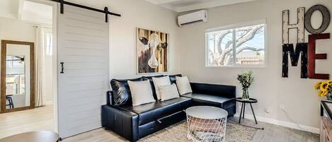 A modern living room with a black leather sofa, a round coffee table, and a large window.