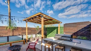 Un patio exterior con una pérgola de madera, una parrilla de barbacoa y zona de estar.