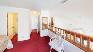 Een ruime kamer met een rood tapijt, een witte stoel en een houten leuning.