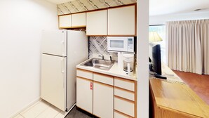 Een kleine keuken met een koelkast, magnetron, spoelbak en koffiezetapparaat.