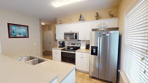 A modern kitchen with white cabinetry, stainless steel appliances, and decorative items on the wall. - Champions Unit 3707 (Sunset Beach)