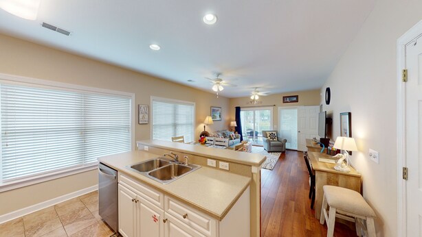 A spacious kitchen with a central island, a dining area with a table and chairs, and a living room with a sofa and a TV. - Champions Unit 3707 (Sunset Beach)