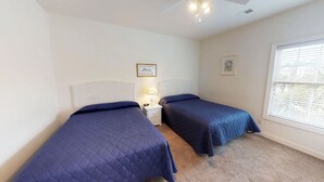 A bedroom with two beds, a nightstand with a lamp, and a window with blinds. - Champions Unit 3612 (Sunset Beach)