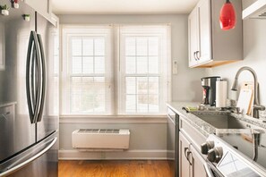 A modern kitchen with a stainless steel refrigerator, a built-in oven, a double sink, and a window with blinds.