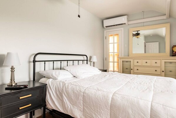A bedroom with a bed, bedside tables, a dresser, a mirror, and an air conditioning unit. - Charming Condo Historic Comfort Access (Hagerstown)