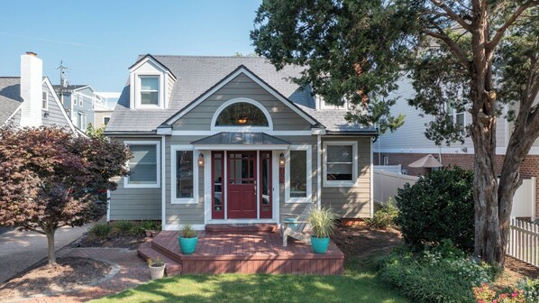 A two-story house with a red front door, a covered porch, and a small front yard with potted plants.