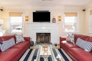 A living room with two red leather sofas, a fireplace, a flat-screen TV, and a striped rug.