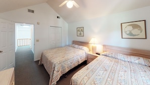 Ein Hotelzimmer mit zwei Betten, einem Nachttisch mit Lampe, einem Deckenventilator und einer Tür zu einem anderen Raum.