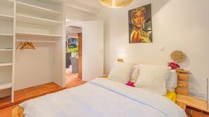 Une chambre à coucher avec un lit, des murs blancs, un tableau, une table de chevet en bois et un luminaire suspendu.