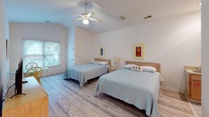 Une chambre d’hôtel avec deux lits, un bureau avec un ordinateur, une chaise, un ventilateur de plafond et une fenêtre avec des stores.