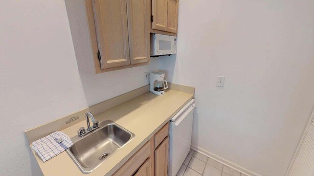 A compact kitchen with a sink, a coffee maker, and wooden cabinets. - Club Villas Unit 17D - Lower Level (Sunset Beach)