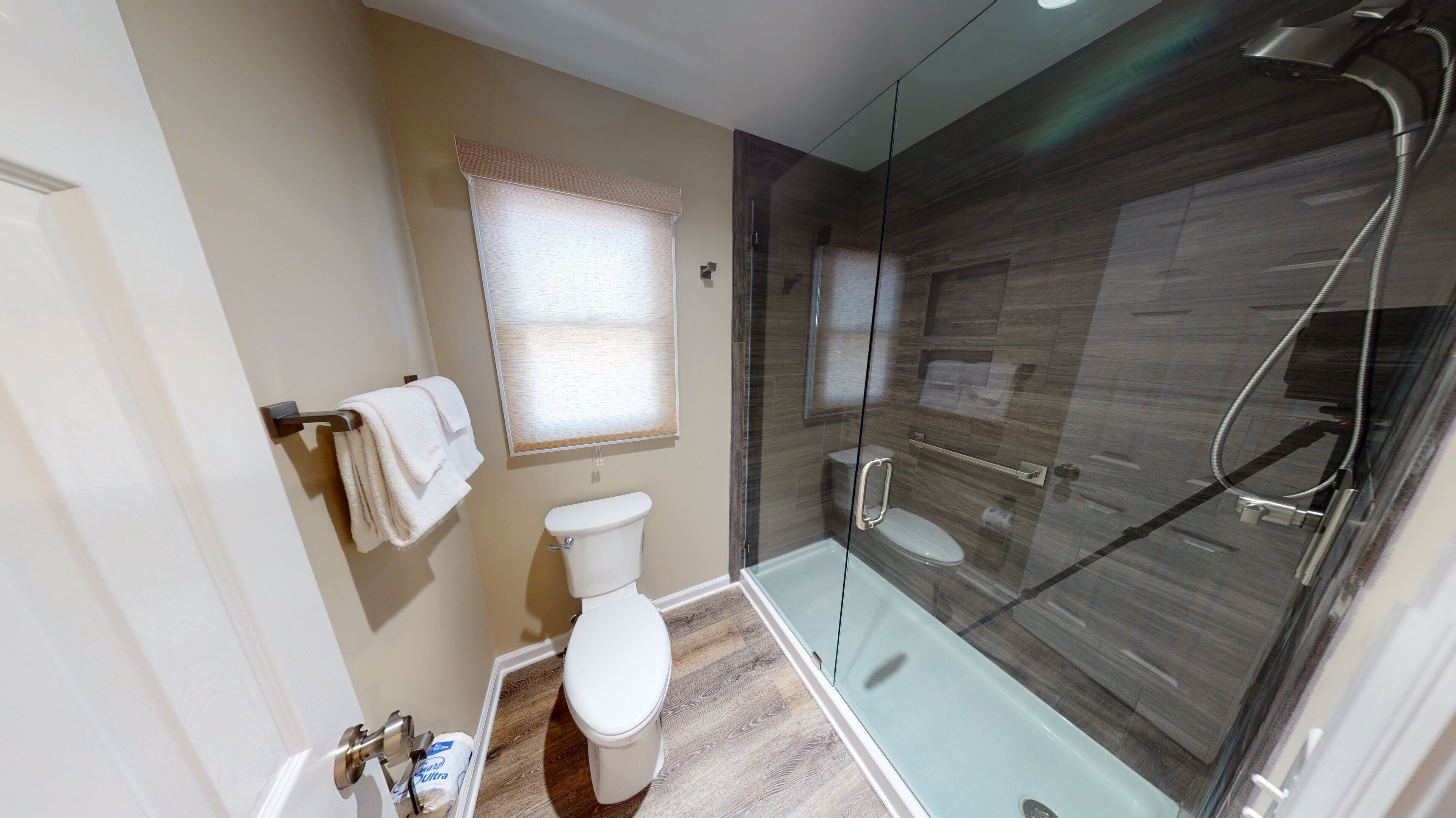 A modern bathroom with a glass-enclosed shower, a toilet, and a towel rack.