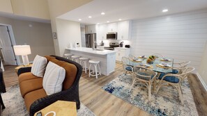 Una cocina moderna con armarios blancos, una isla central y un comedor con mesa de vidrio y sillas de mimbre.
