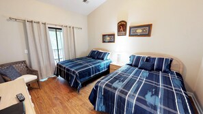 A bedroom with two beds, a wooden chair, a window with curtains, and two framed pictures on the wall. - Club Villas Unit 19C Villa (Sunset Beach)