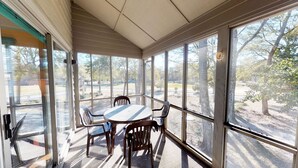 Aurinkoinen huone, jossa on pöytä ja tuoleja, suuret ikkunat sekä näkymä puille ja parkkipaikalle.