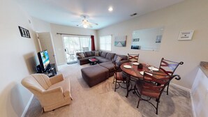 A living room with a sectional sofa, a dining table with chairs, a TV, and a ceiling fan. - Champions Unit 3417 (Sunset Beach)