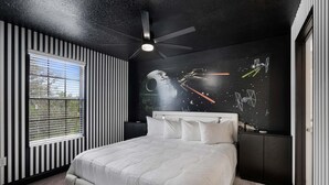 Un dormitorio con cama, ventilador de techo, ventana con persianas y una pared decorada con ilustraciones de Star Wars.