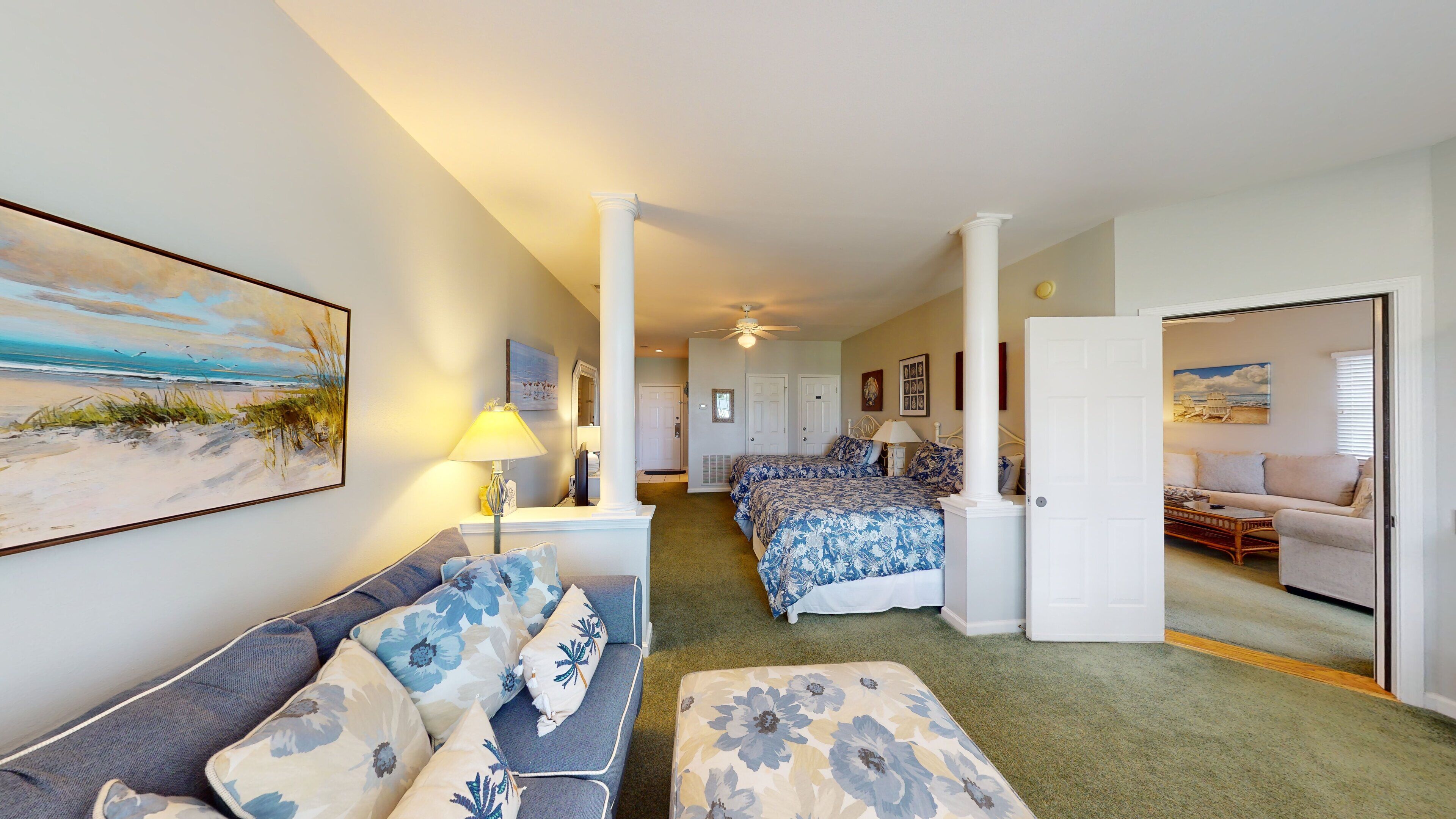 A bedroom with a bed, a sofa, and a painting of a beach scene.