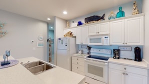 A modern kitchen with white cabinetry, a built-in microwave, a stove, and a sink. - Champions Unit 3509 (Sunset Beach)