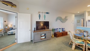 A living room with a flat-screen TV, a wooden coffee table, and a dining area with wicker chairs. - Champions Unit 3509 (Sunset Beach)