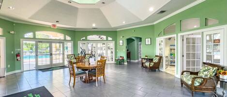 A spacious lobby with a high ceiling, a central dining area, and a seating area with wicker furniture.