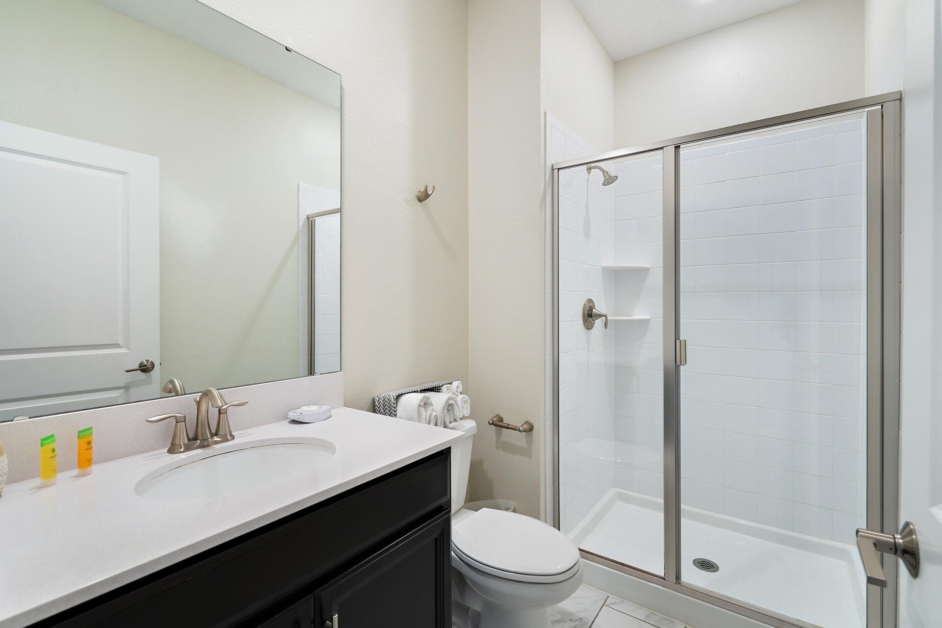 A modern bathroom with a white sink, a toilet, a glass-enclosed shower, and a large mirror.