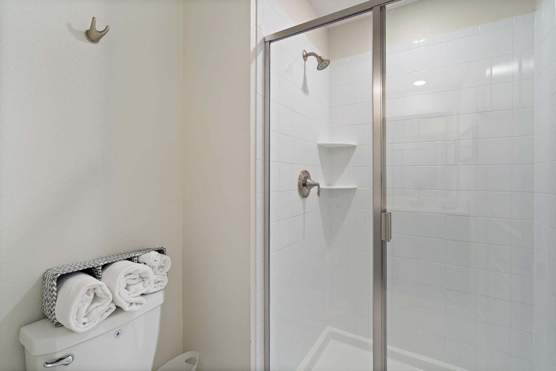A bathroom with a glass shower enclosure, white tiled walls, a toilet with a towel rack, and a shower head.