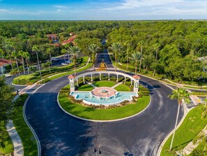 Una glorieta ajardinada con una fuente central, rodeada de palmeras y una carretera.