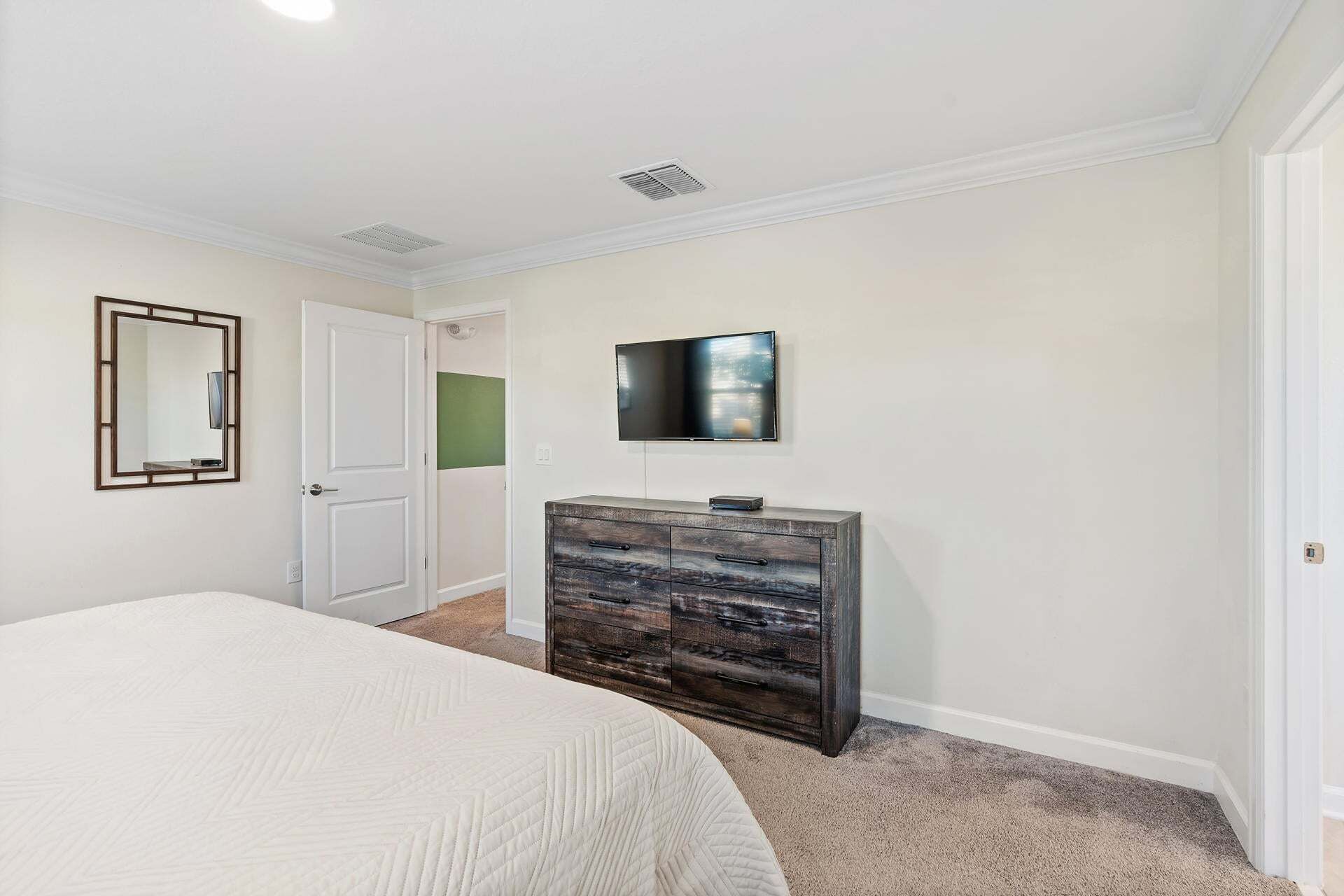 A bedroom with a bed, a dresser, a television, and a door leading to another room.